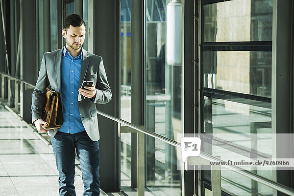 Young businessman walking looking on cell phone