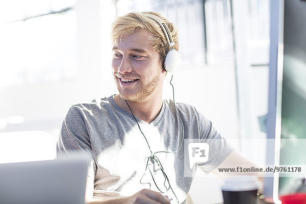 Kreativer Büromann  der am Computer arbeitet und ein Headset trägt.