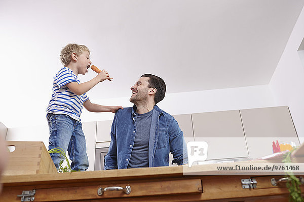 Vater und Sohn in der Küche  Junge singt auf dem Tisch und hält Carrogt.