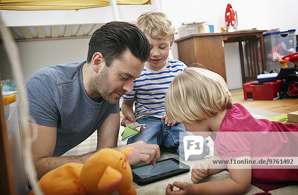 Father and children using mini tablet  lying on floor