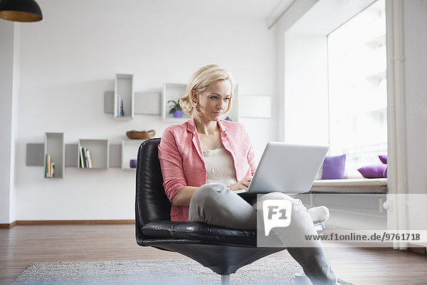 Woman sitting with laptop on leather chair at home