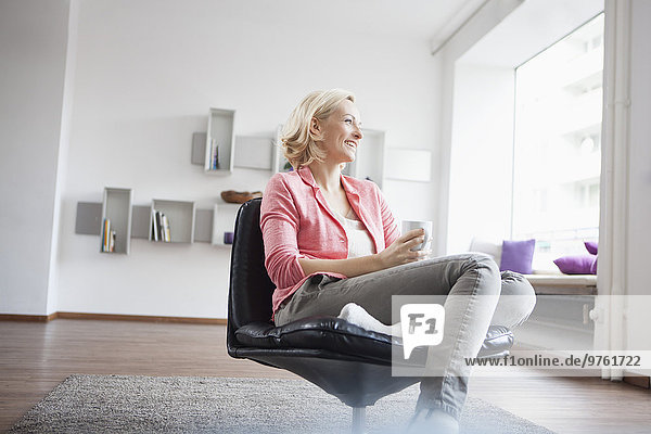 Woman with cup of tea relaxing on leather chair at home