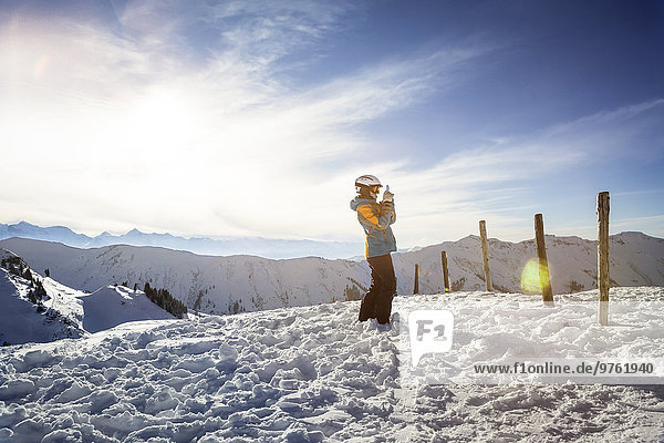 Österreich  Land Salzburg  Region Hochkönig  junge Skifahrerin beim Fotografieren mit Smartphone