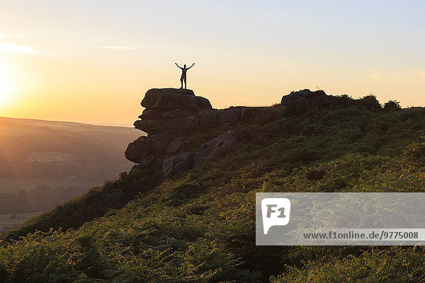 On top of the world  visitor enjoys sunset on Curbar Edge with arms aloft  Peak District National Park  Derbyshire  England  United Kingdom  Europe