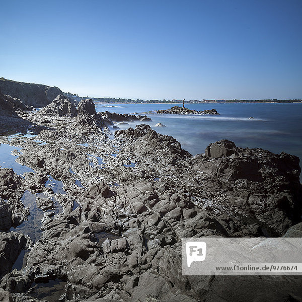 Rocky beach at low tide with man fishing on rock  Argelles  France  Europe