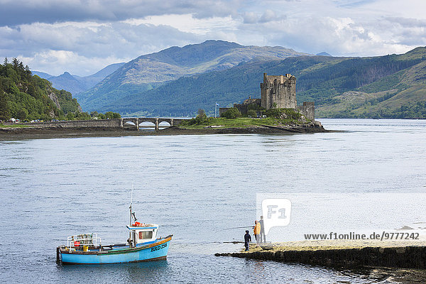 Fishermen fishing by Eilean Donan Castle  a Highland fortress  with Saltire Scottish flag flying in Loch Alsh at Dornie  Kyle of Lochalsh in the western hIghlands of Scotland  United Kingdom  Europe