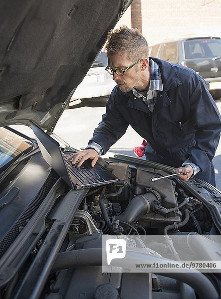 Mechanic using laptop while repairing car