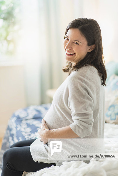Pregnant woman holding ultrasound  sitting on bed smiling