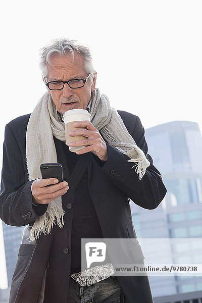 Man in street drinking coffee using smartphone