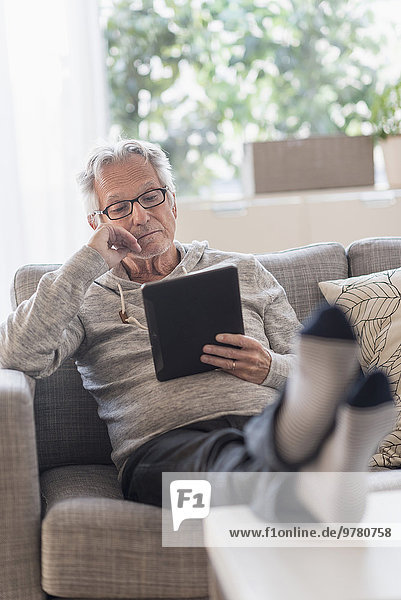 Senior man sitting on couch in living room and using tablet pc