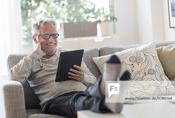 Senior man sitting on couch in living room  using tablet pc and smiling