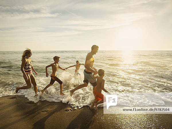 Family with three children (6-7  10-11  14-15) running on beach