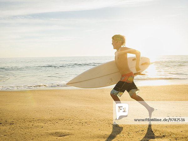 Teenage boy (14-15) with surfboard running on beach