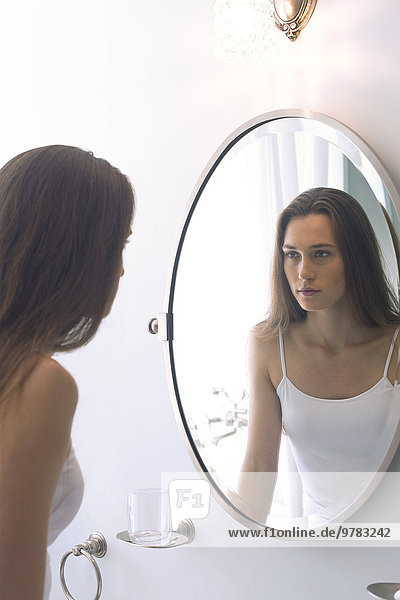 Woman looking at self in bathroom mirror