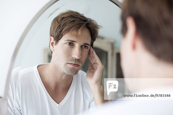 Mann schaut sich selbst im Spiegel an mit besorgtem Blick