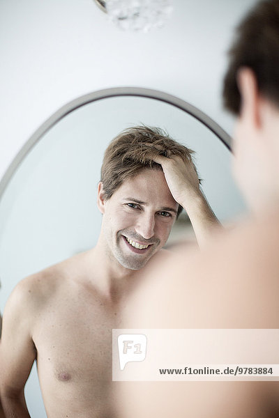 Mann mit Händen im Haar  der sich selbst im Spiegel ansieht und sich amüsiert.