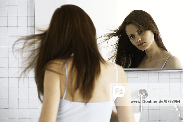 Junge Frau schaut in den Spiegel  trocknet die Haare.