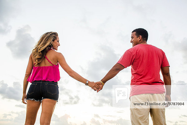 Low angle view of couple holding hands under cloudy sky