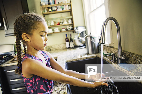 Mixed race girl washing hands in kitchen sink