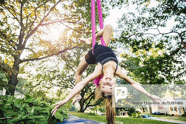 Acrobatic Caucasian girl hanging on fabric under tree
