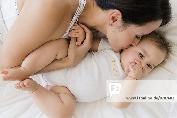 Overhead view of mixed race mother kissing baby on bed