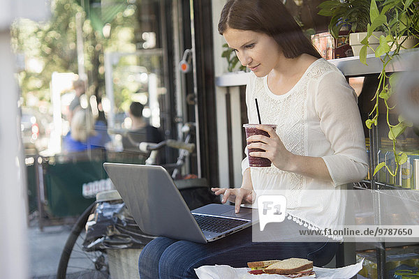 Caucasian woman using laptop and drinking coffee outside cafe