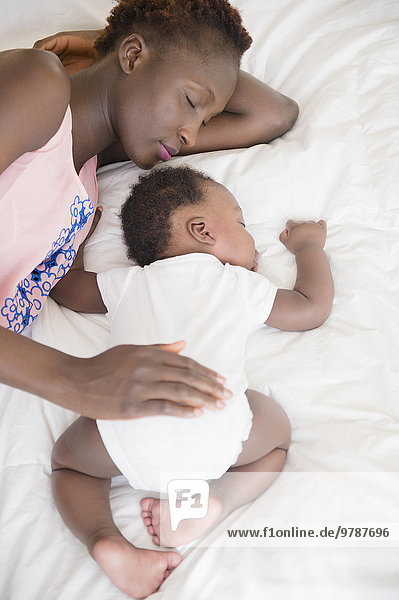 Black mother and son sleeping on bed