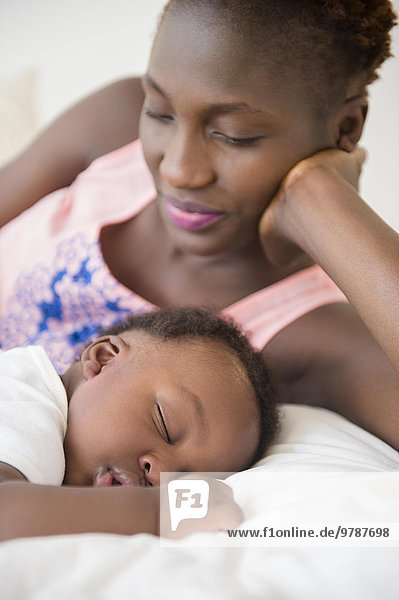 Black mother admiring sleeping son on bed