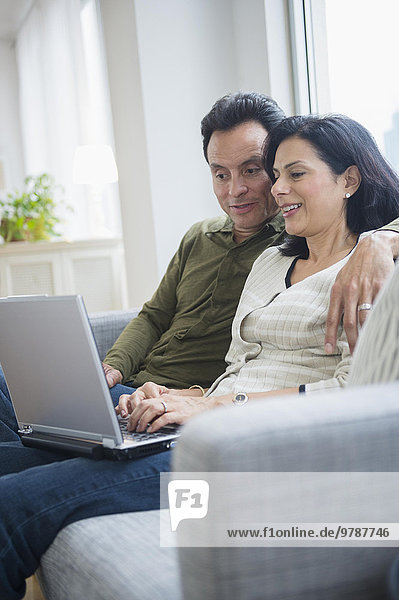 Couple using laptop on sofa in living room