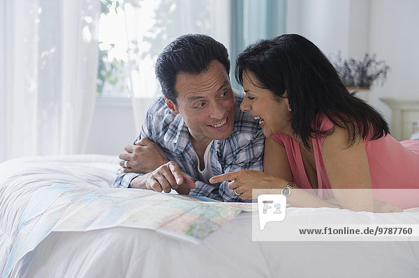Couple reading map on bed