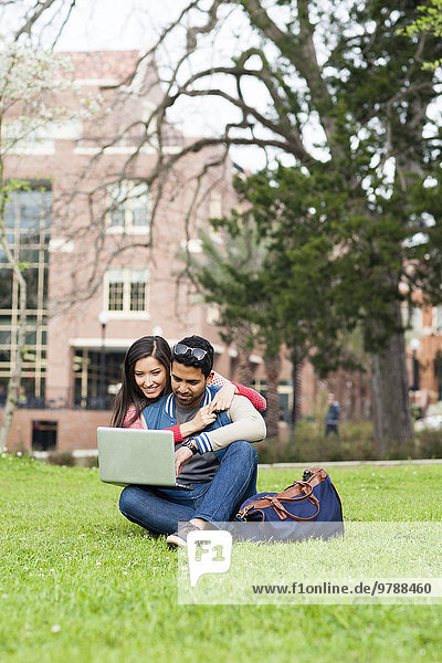 Students hugging and using laptop on campus