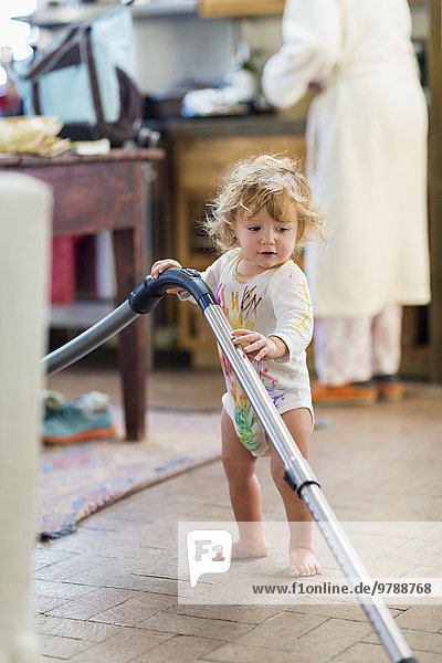 Caucasian baby boy vacuuming in kitchen