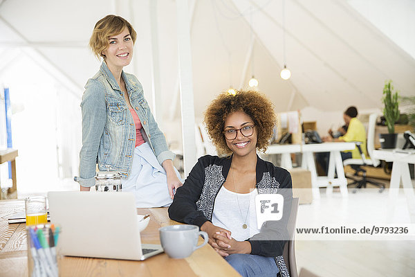 Portrait von lächelnden Frauen im Büro mit Laptop auf dem Schreibtisch