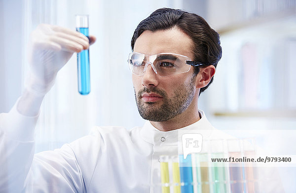 Man in laboratory looking at vial with blue fluid