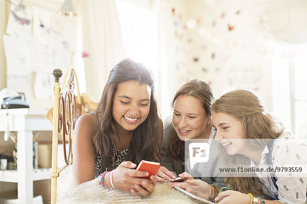 Drei Mädchen im Teenageralter, die zusammen auf dem Bett im Schlafzimmer liegen und ein Smartphone benutzen.