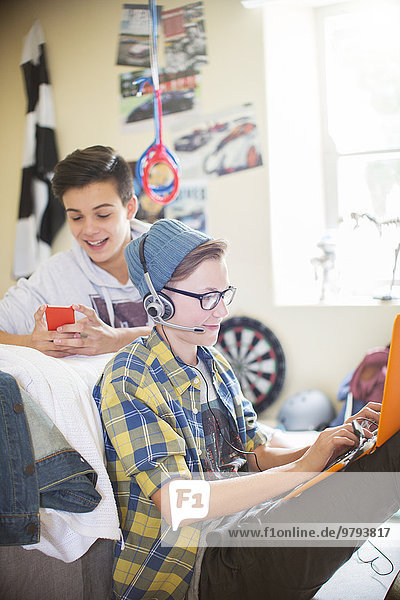 Zwei Teenager, die elektronische Geräte im Zimmer benutzen.