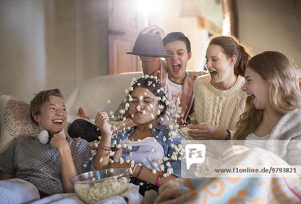 Gruppe von Jugendlichen, die Popcorn auf sich selbst werfen, während sie auf dem Sofa sitzen.