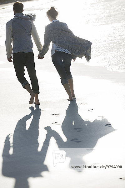 Young couple holding hands and walking on beach