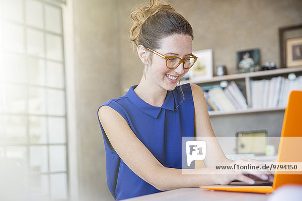 Porträt einer jungen Frau mit orangefarbenem Laptop bei der Arbeit im Home Office