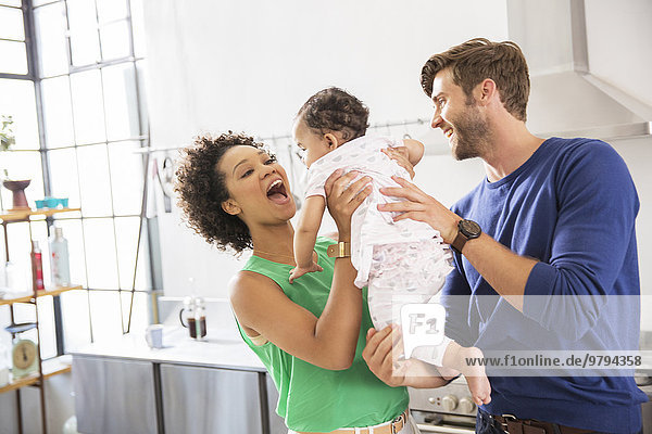 Happy parents holding their baby daughter in domestic kitchen
