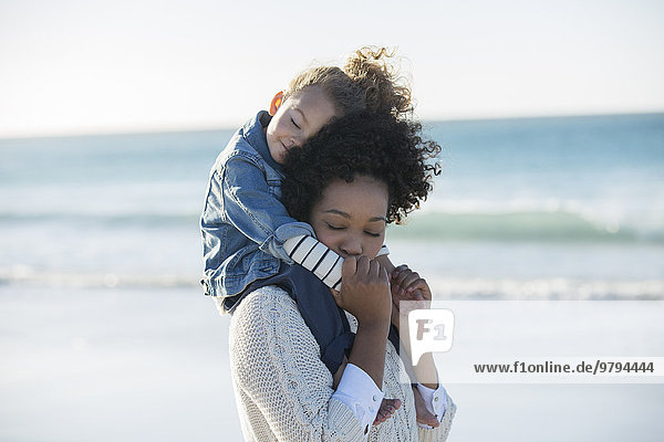 Mutter mit Tochter auf den Schultern am Strand