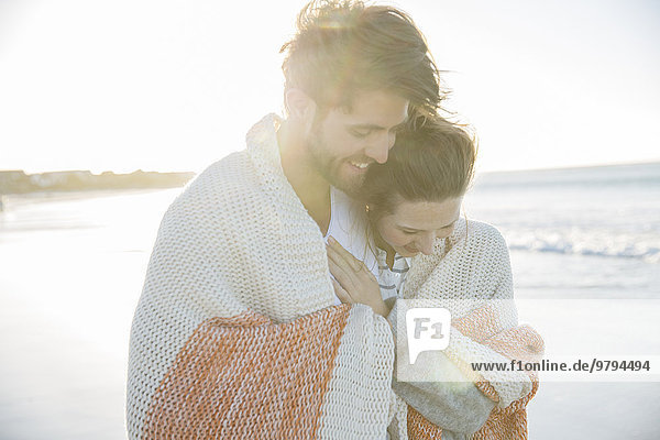 Young couple wrapped in blanket on beach