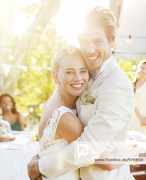 Porträt eines jungen Paares  das sich während der Hochzeitsfeier im Garten umarmt.