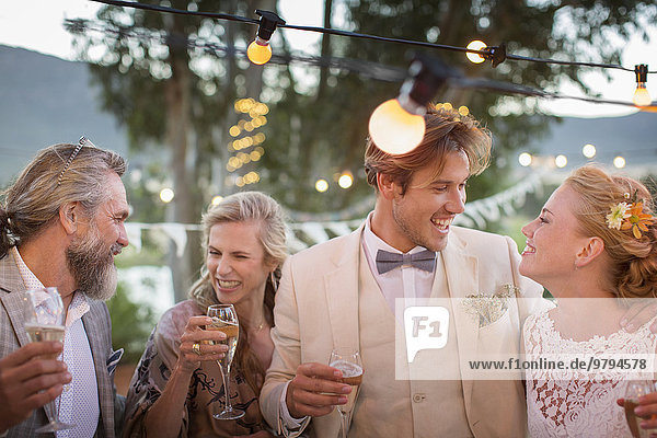 Young couple and their guests with champagne flutes during wedding reception in garden