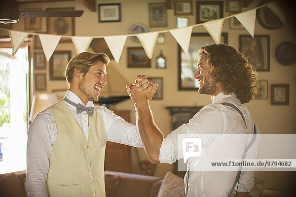 Bridegroom and best man holding hands in domestic room