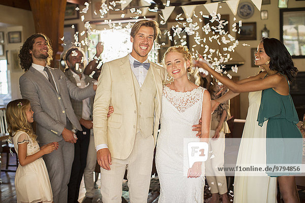 Porträt eines lächelnden jungen Paares im fallenden Konfetti während des Hochzeitsempfangs
