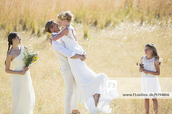 Bridesmaid and bridesmaid watching and laughing Young couple embracing in meadow