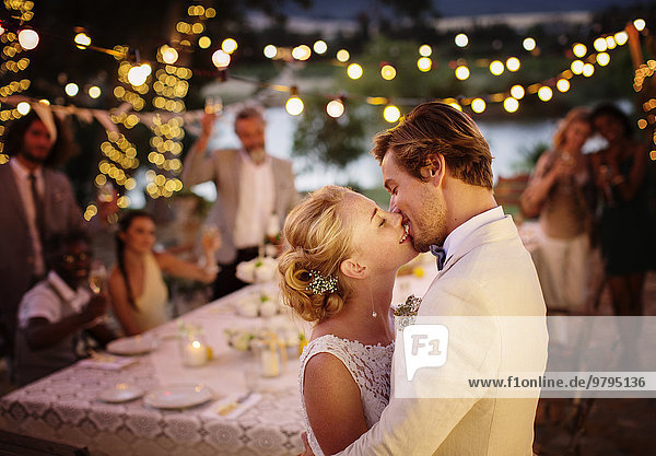 Junge Paare küssen sich während der Hochzeitsfeier im Hausgarten