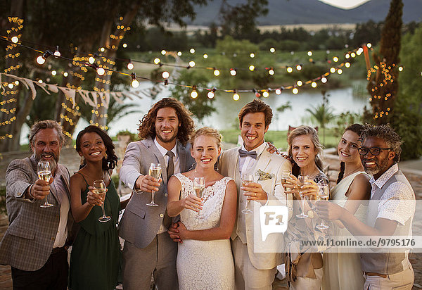Portrait of young couple with guests toasting with champagne during wedding reception at dusk