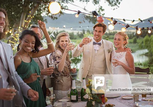 Young couple and guests toasting with champagne during wedding reception in domestic garden